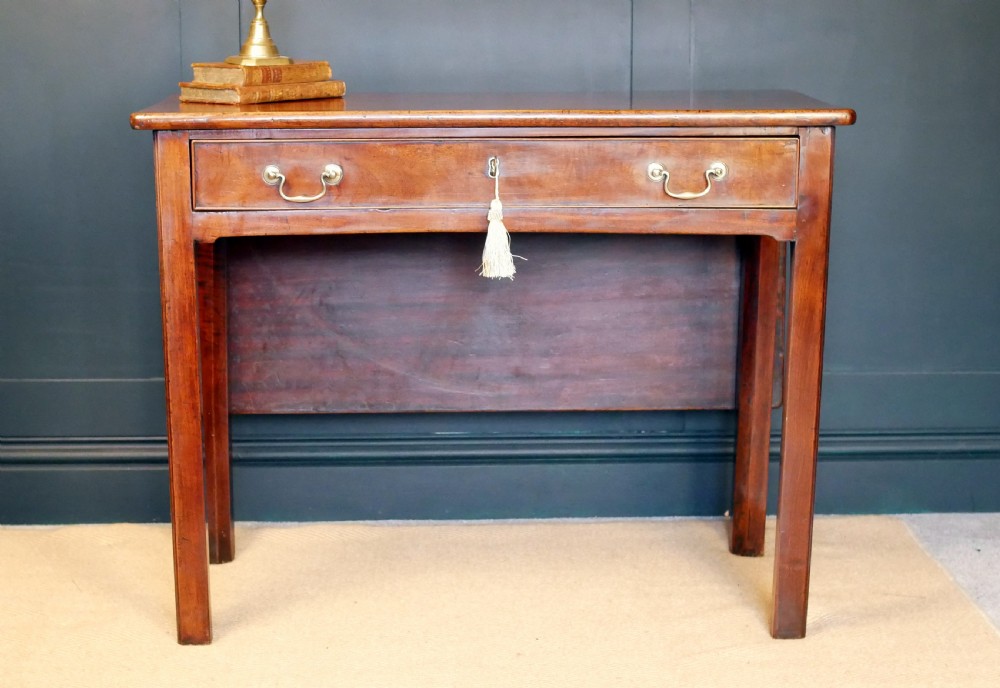 A George IV mahogany console table with a single frieze drawer, brass swan-neck handles, key tassel, and straight square legs. View IV