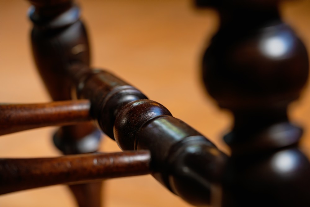 A dark brown wooden captains chair featuring a curved crest rail, turned spindles, a contoured saddle seat, and turned legs joined by stretchers. View VIII