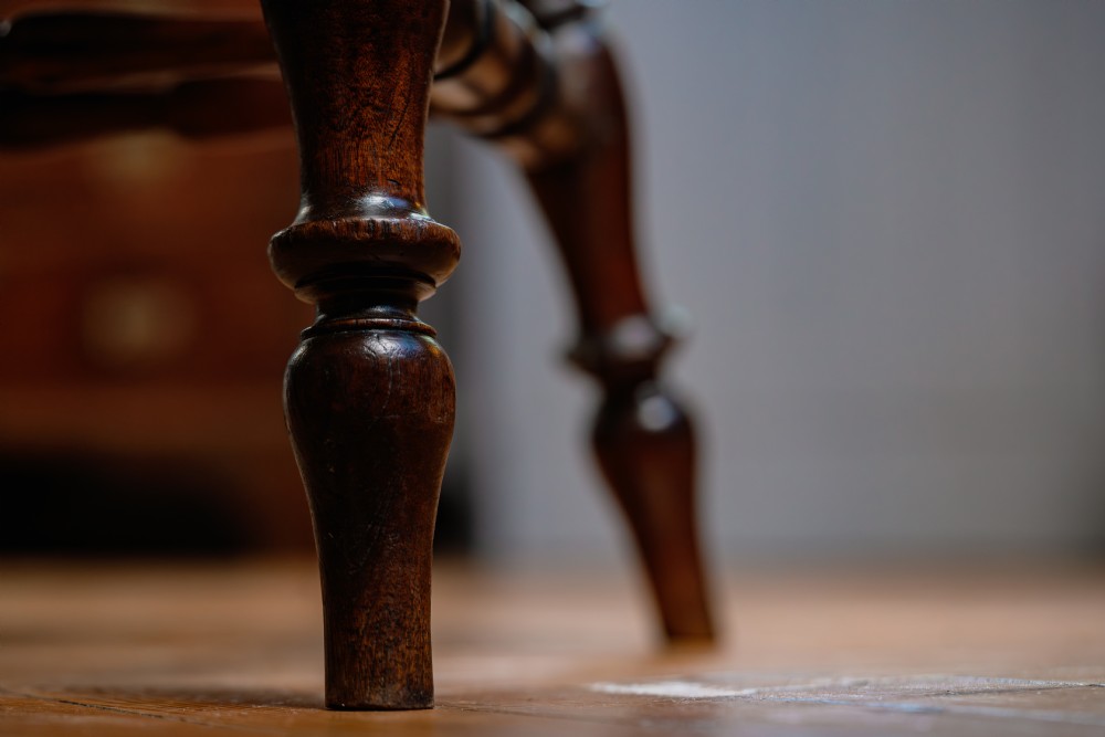A dark brown wooden captains chair featuring a curved crest rail, turned spindles, a contoured saddle seat, and turned legs joined by stretchers. View IX