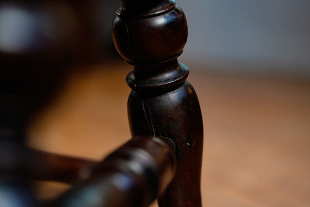 A dark brown wooden captains chair featuring a curved crest rail, turned spindles, a contoured saddle seat, and turned legs joined by stretchers. View XI