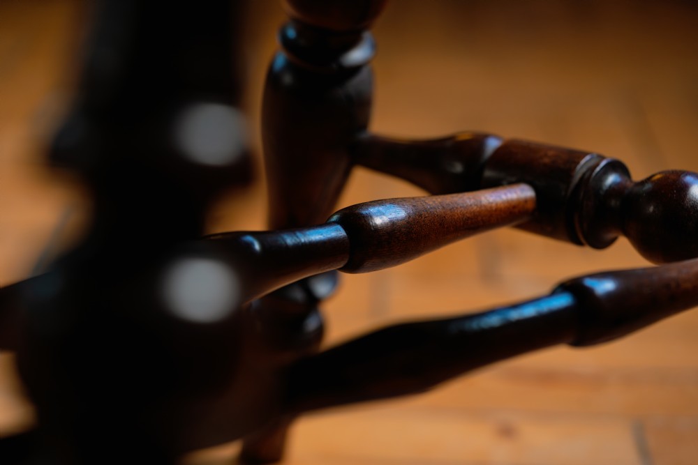A dark brown wooden captains chair featuring a curved crest rail, turned spindles, a contoured saddle seat, and turned legs joined by stretchers. View XII