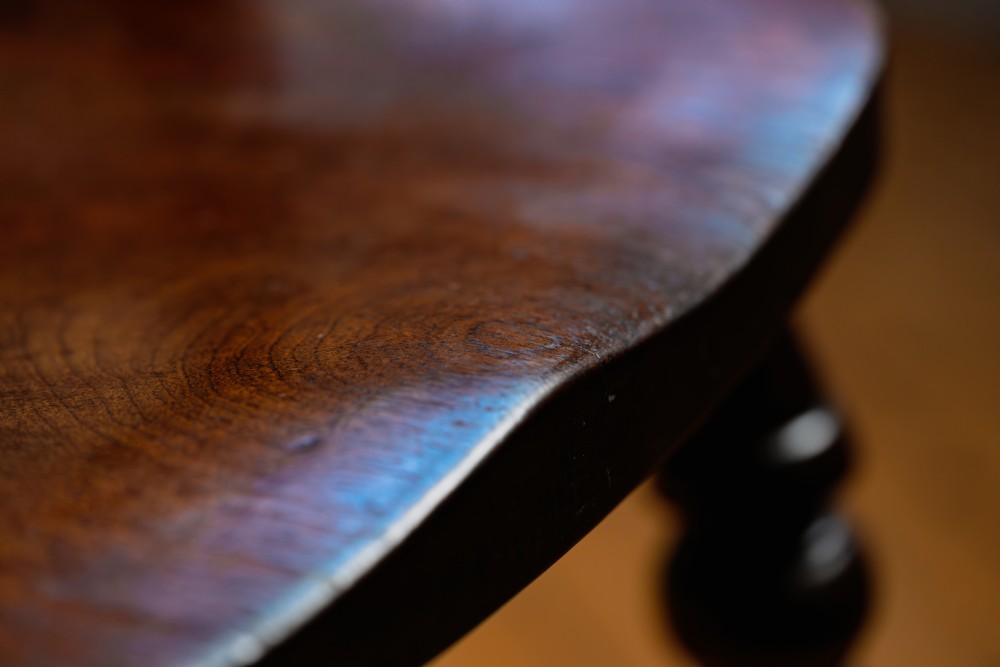 A dark brown wooden captains chair featuring a curved crest rail, turned spindles, a contoured saddle seat, and turned legs joined by stretchers. View XIII