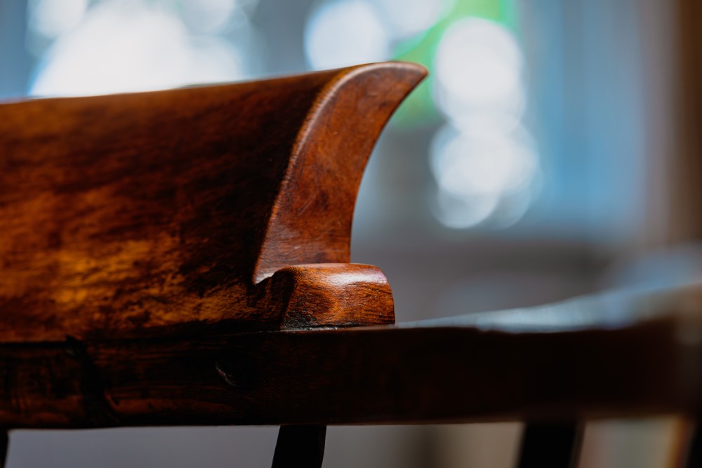 A dark brown wooden captains chair featuring a curved crest rail, turned spindles, a contoured saddle seat, and turned legs joined by stretchers. View XV