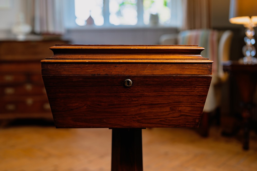A Victorian rosewood teapoy featuring a rectangular hinged box top with a keyhole, supported by a tapered pedestal column on a four-pointed plinth base with scroll feet. View III