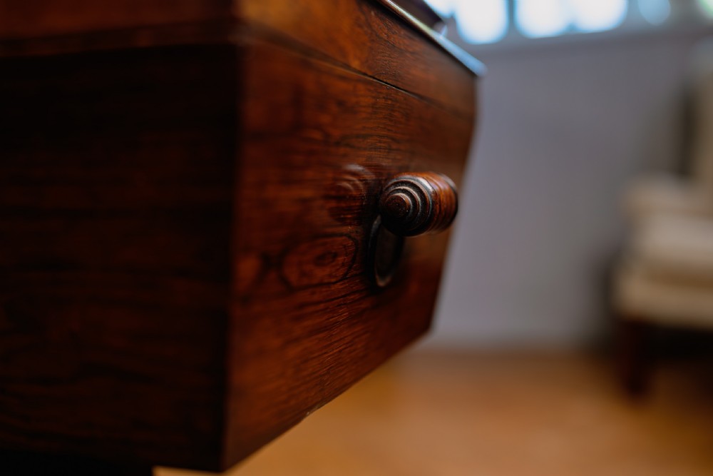 A Victorian rosewood teapoy featuring a rectangular hinged box top with a keyhole, supported by a tapered pedestal column on a four-pointed plinth base with scroll feet. View IV