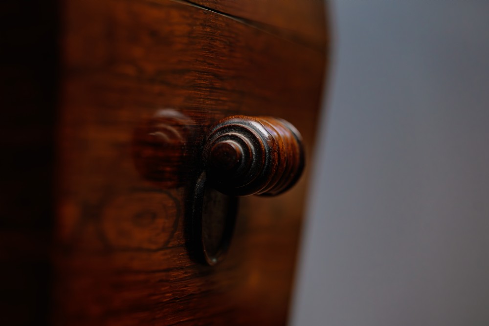 A Victorian rosewood teapoy featuring a rectangular hinged box top with a keyhole, supported by a tapered pedestal column on a four-pointed plinth base with scroll feet. View V