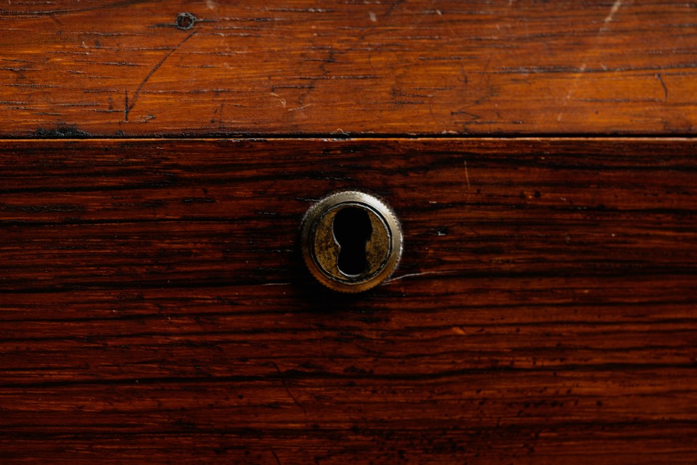 A Victorian rosewood teapoy featuring a rectangular hinged box top with a keyhole, supported by a tapered pedestal column on a four-pointed plinth base with scroll feet. View VI