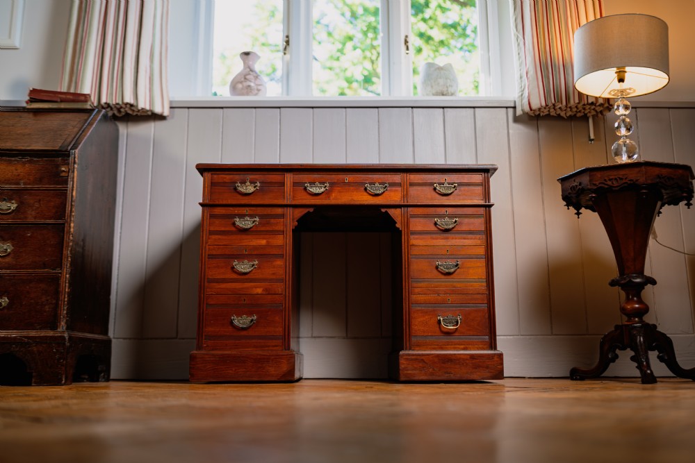 An antique warm brown walnut pedestal desk featuring nine drawers with brass handles and reeded moulding around a central kneehole.