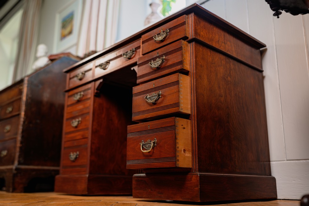 An antique warm brown walnut pedestal desk featuring nine drawers with brass handles and reeded moulding around a central kneehole. View II