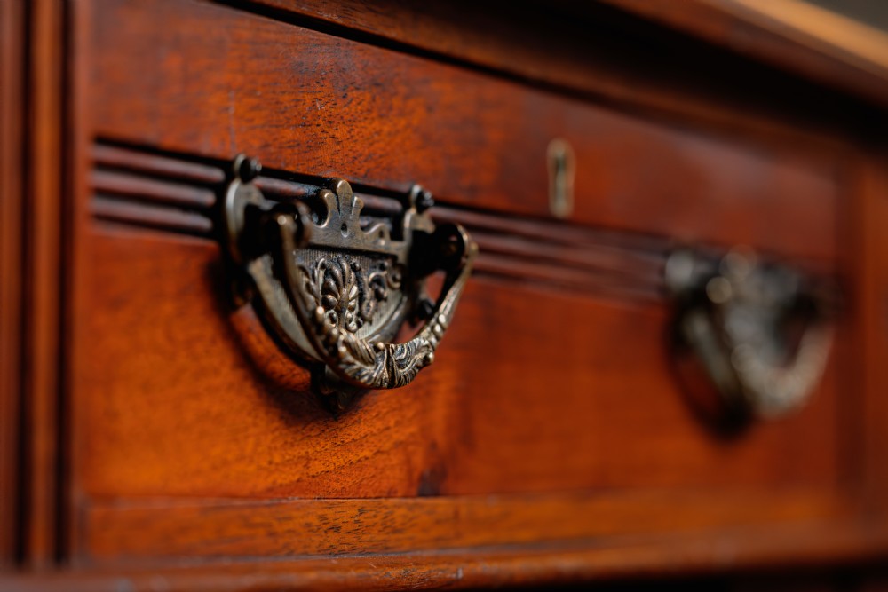 An antique warm brown walnut pedestal desk featuring nine drawers with brass handles and reeded moulding around a central kneehole. View IV