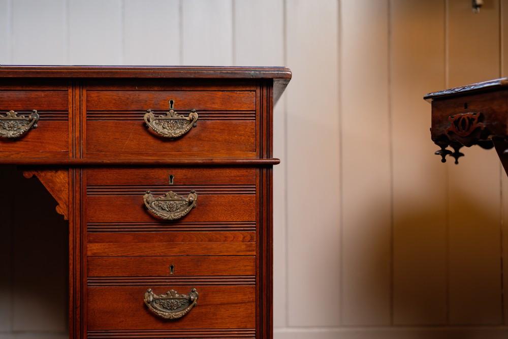 An antique warm brown walnut pedestal desk featuring nine drawers with brass handles and reeded moulding around a central kneehole. View VI