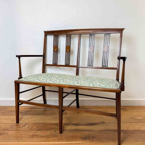 fig 1. An Edwardian mahogany settee featuring an inlaid open back, straight legs with stretchers, and a patterned fabric upholstered seat.