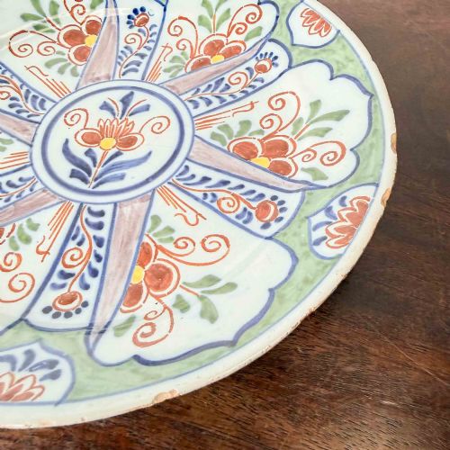 fig 1. An antique circular tin-glazed earthenware plate decorated with hand-painted floral and geometric motifs in orange, cobalt blue, and brown over a pale green background.