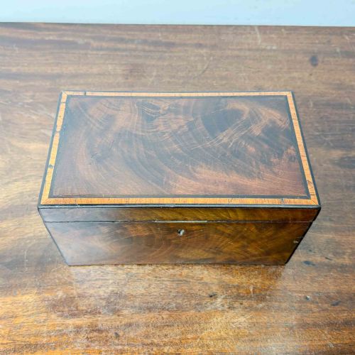 fig 2. A rectangular early Victorian tea caddy crafted from flame mahogany veneer with crossbanded inlaid borders and a central metal keyhole escutcheon.