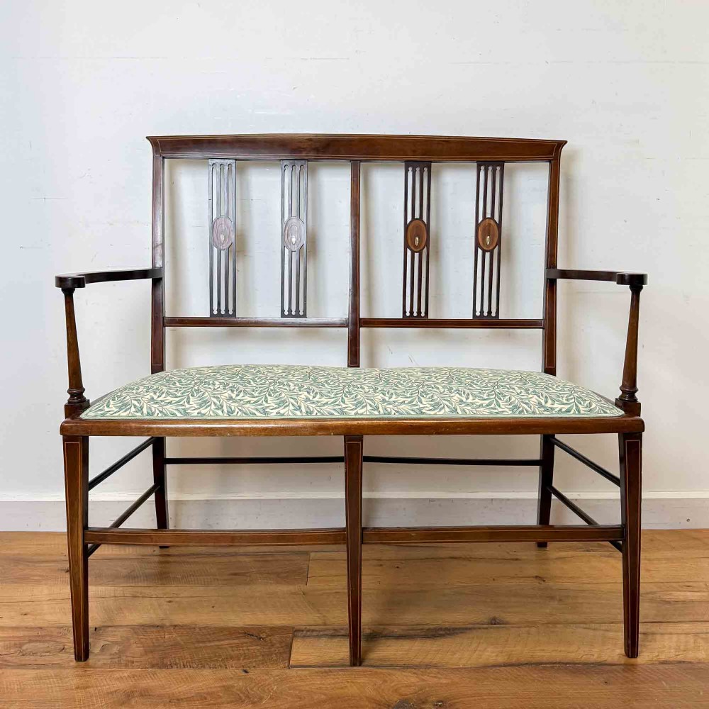 An Edwardian mahogany settee featuring an inlaid open back, straight legs with stretchers, and a patterned fabric upholstered seat.