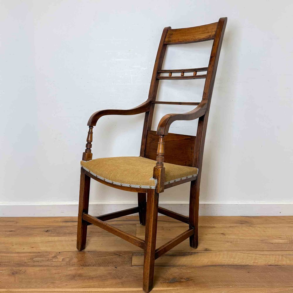 A Regency period high back open armchair crafted from fruitwood and elm with turned arm supports and a textured ochre upholstered seat.