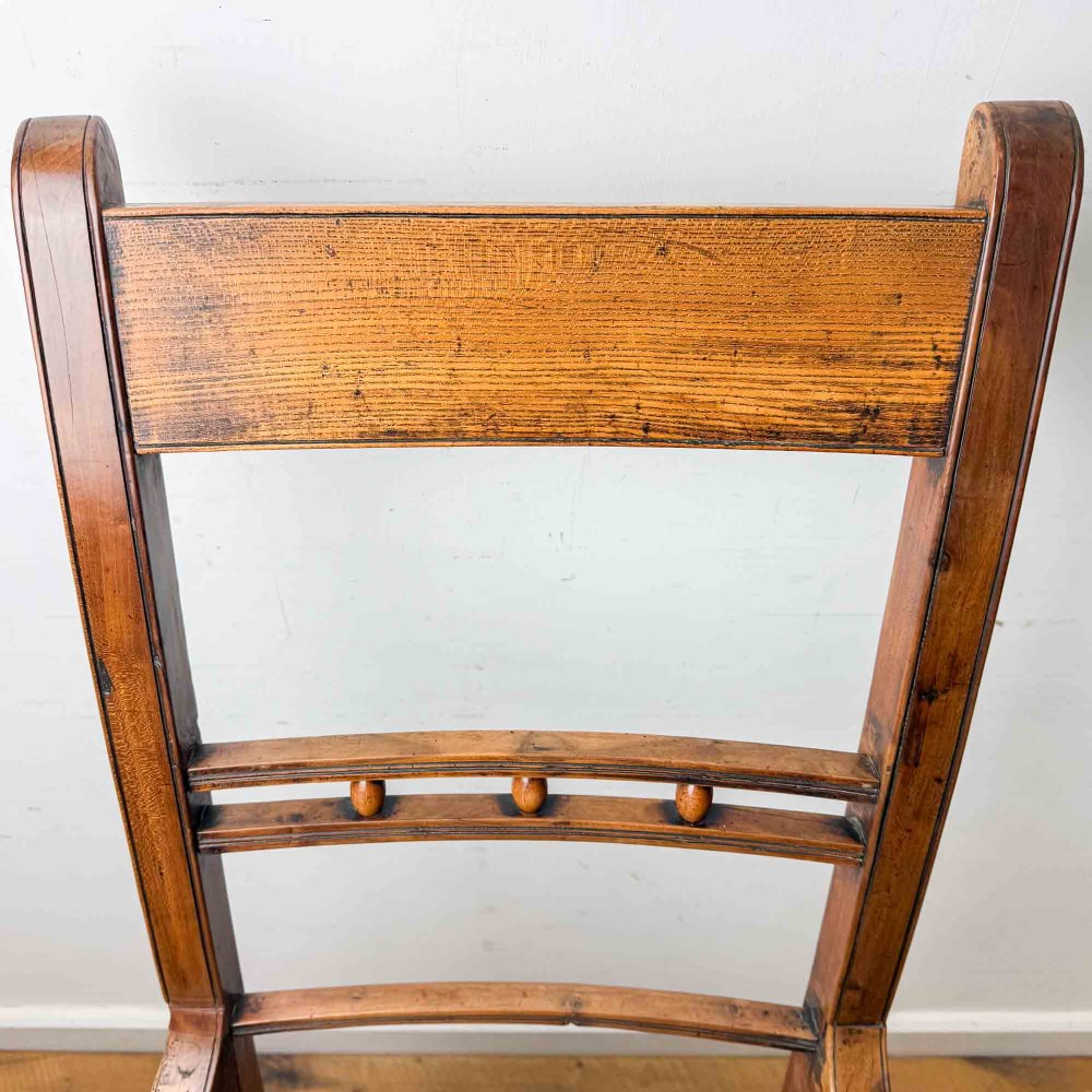 A Regency period high back open armchair crafted from fruitwood and elm with turned arm supports and a textured ochre upholstered seat. View XV