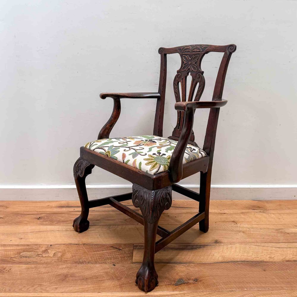 A dark carved oak armchair with cabriole legs, ball and claw feet, a carved splat back, and a crewelwork embroidered seat pad.