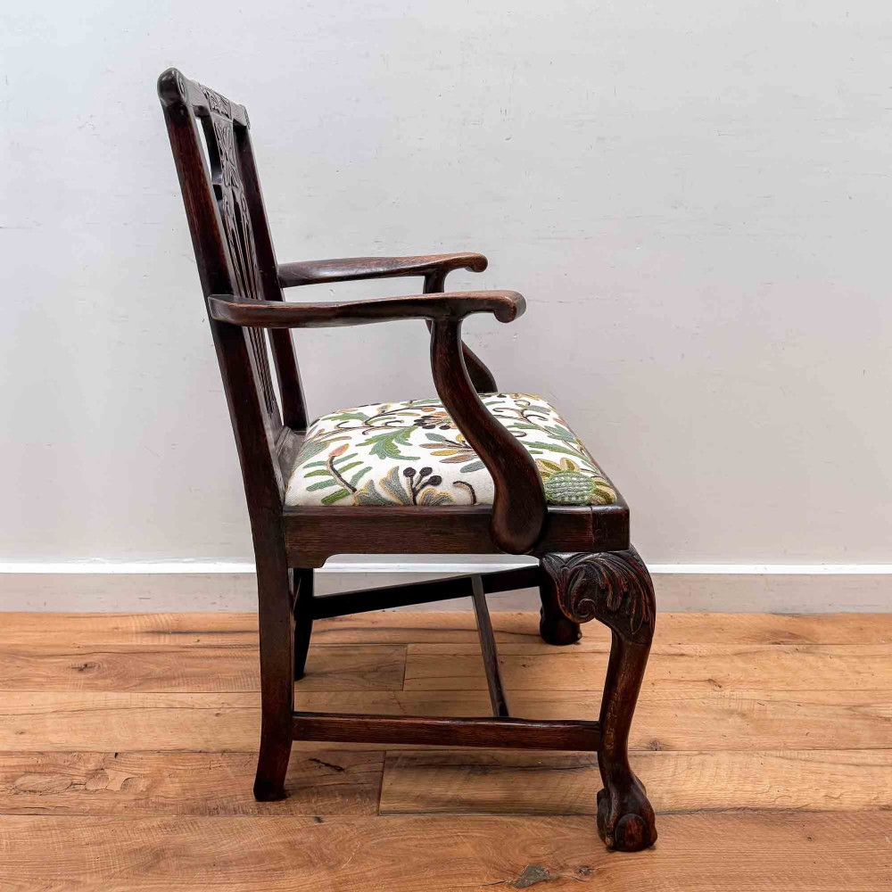 A dark carved oak armchair with cabriole legs, ball and claw feet, a carved splat back, and a crewelwork embroidered seat pad. View IX