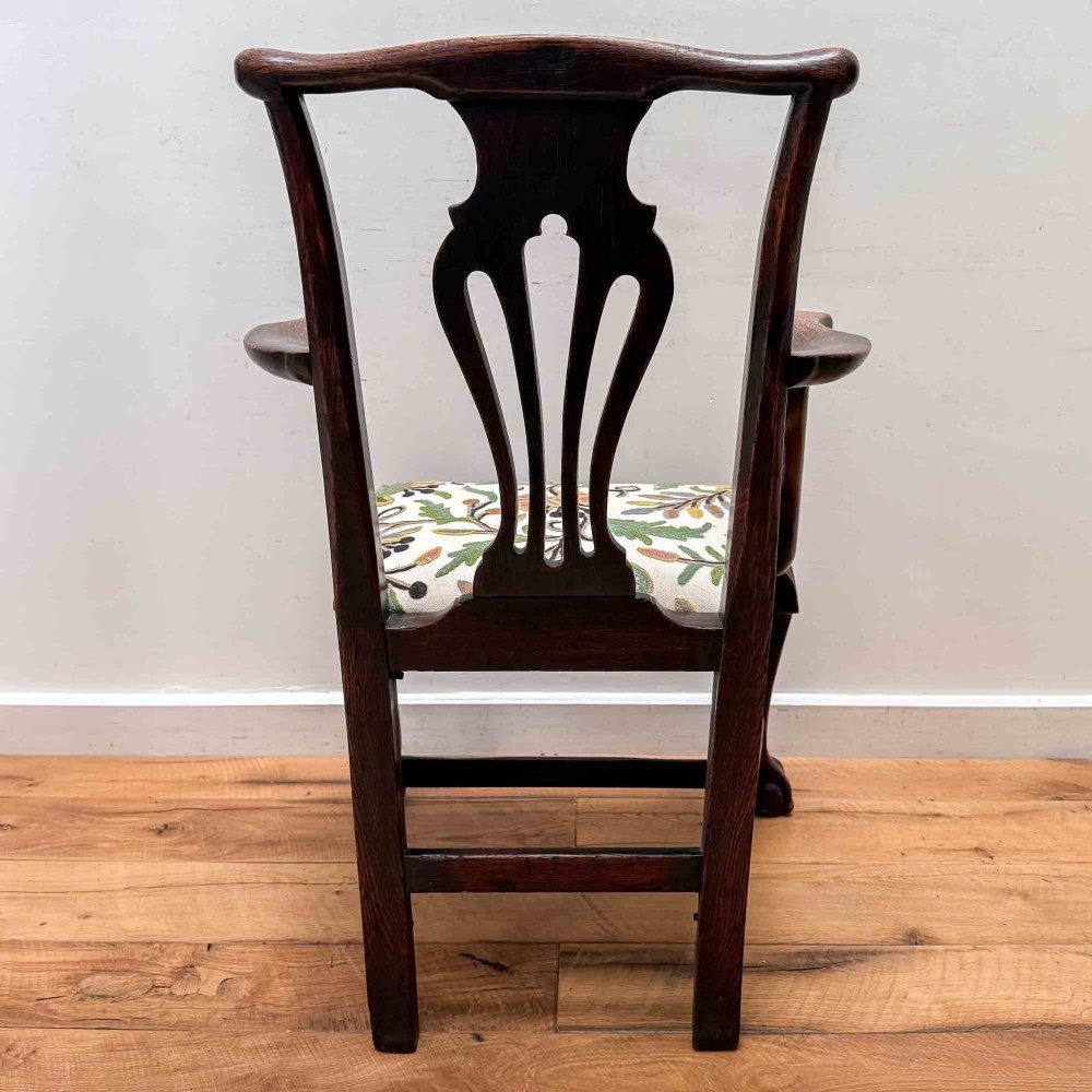 A dark carved oak armchair with cabriole legs, ball and claw feet, a carved splat back, and a crewelwork embroidered seat pad. View X