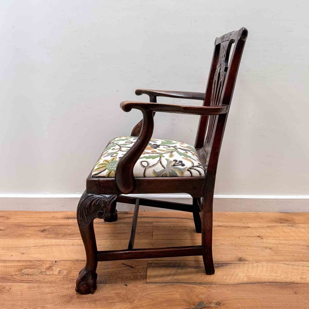 A dark carved oak armchair with cabriole legs, ball and claw feet, a carved splat back, and a crewelwork embroidered seat pad. View XI