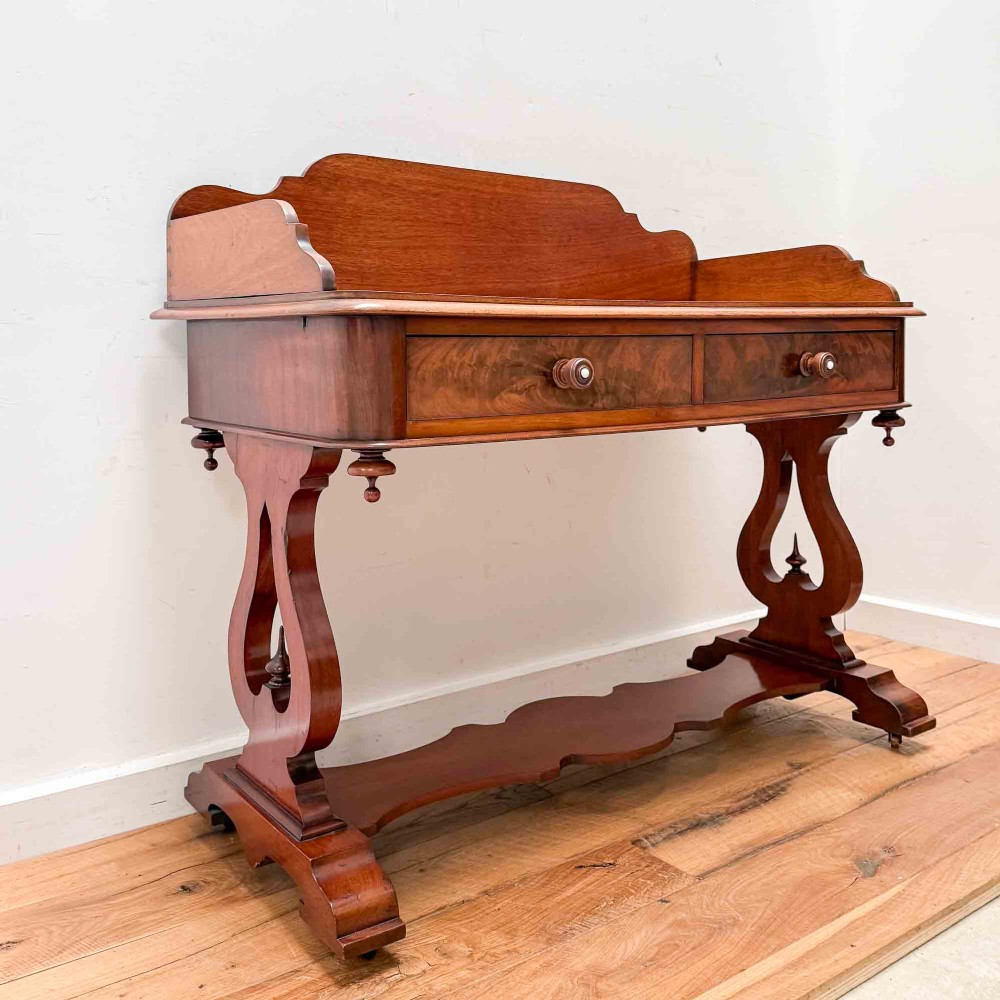 A Victorian mahogany writing table featuring a raised gallery back, two drawer fronts with wooden knobs, shaped lyre supports, and a low stretcher base on castors.