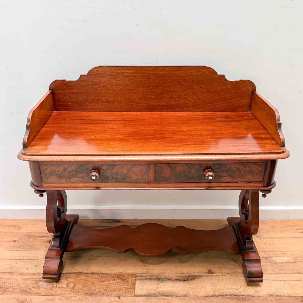 A Victorian mahogany writing table featuring a raised gallery back, two drawer fronts with wooden knobs, shaped lyre supports, and a low stretcher base on castors. View IV