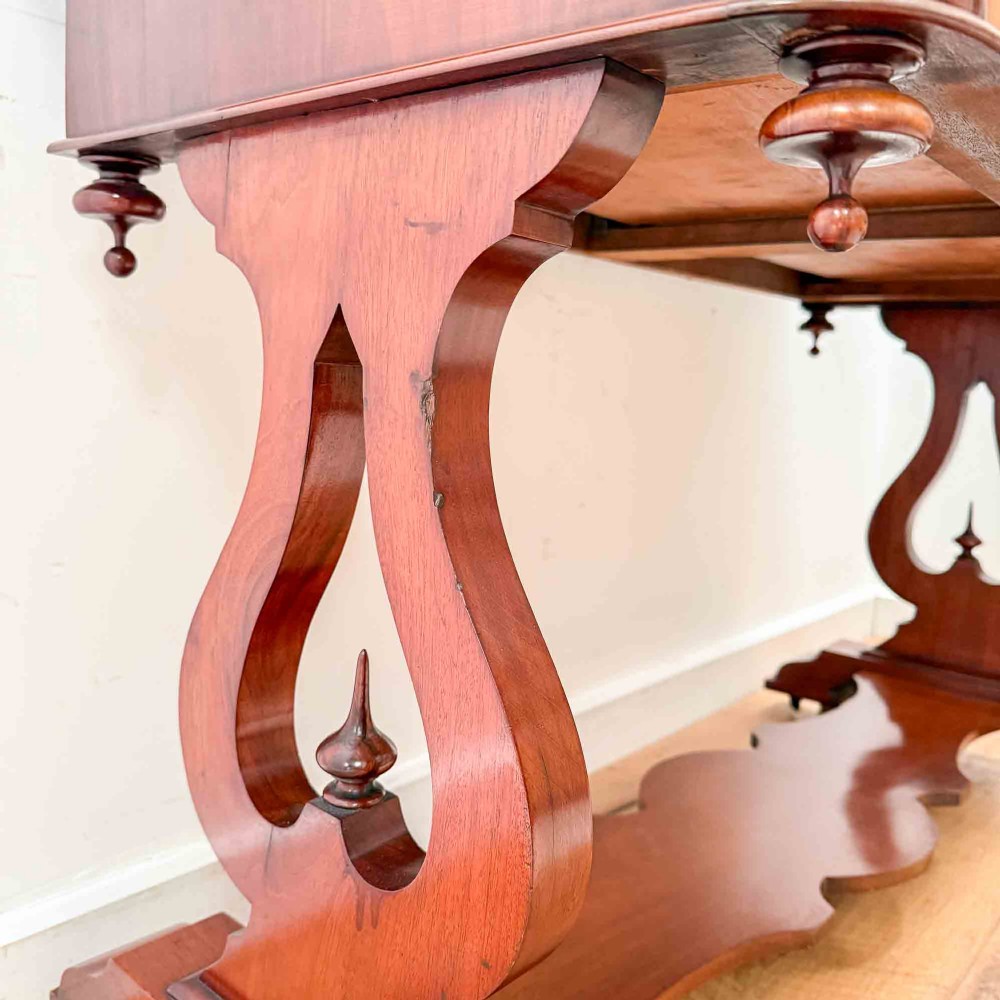 A Victorian mahogany writing table featuring a raised gallery back, two drawer fronts with wooden knobs, shaped lyre supports, and a low stretcher base on castors. View VI