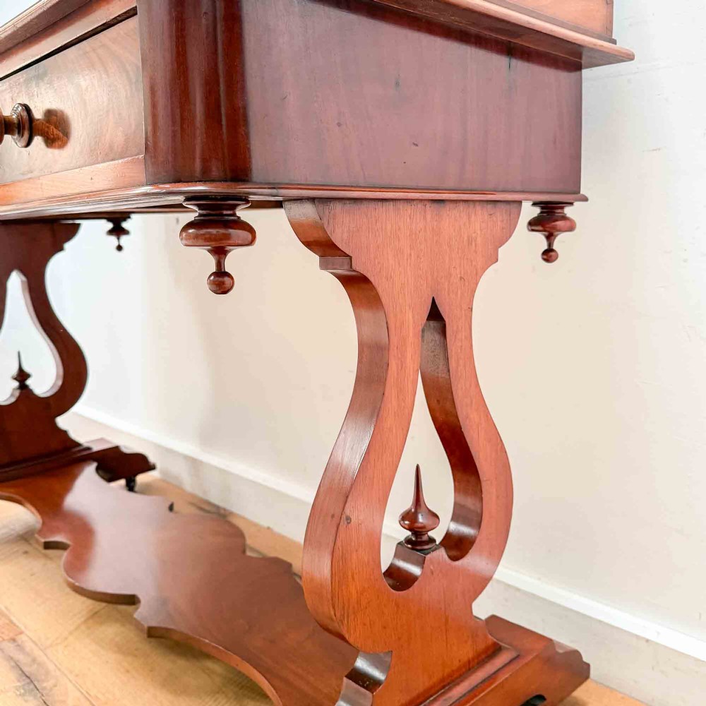 A Victorian mahogany writing table featuring a raised gallery back, two drawer fronts with wooden knobs, shaped lyre supports, and a low stretcher base on castors. View VIII