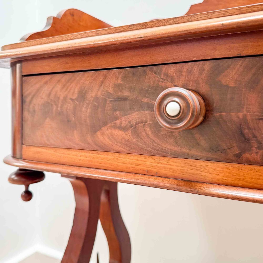A Victorian mahogany writing table featuring a raised gallery back, two drawer fronts with wooden knobs, shaped lyre supports, and a low stretcher base on castors. View XV