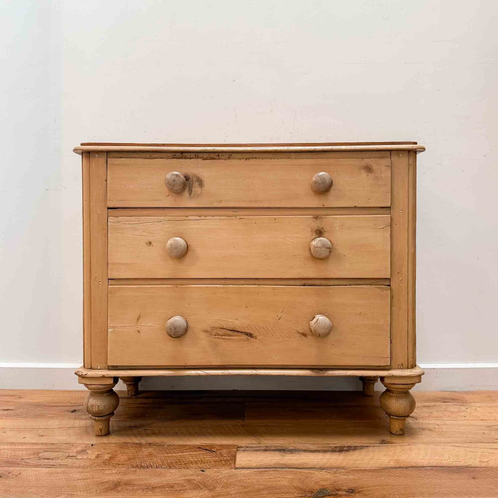 A natural light pine chest of drawers featuring three full-width drawers with turned wooden knobs, rounded front column edges, and turned bun feet.