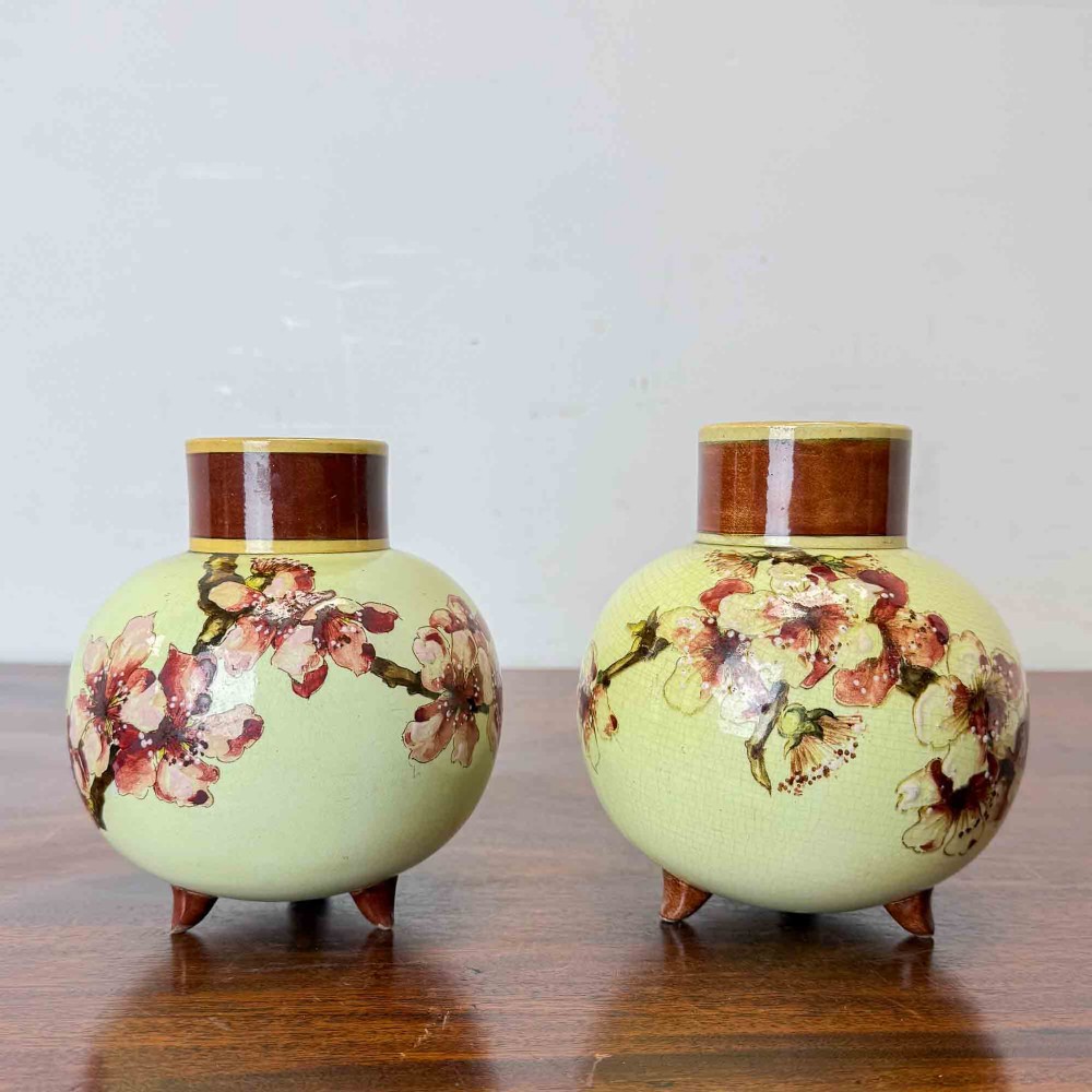 A pair of round pale green ceramic vases with hand-painted pink cherry blossom branches, dark brown collars, and small tripod feet.