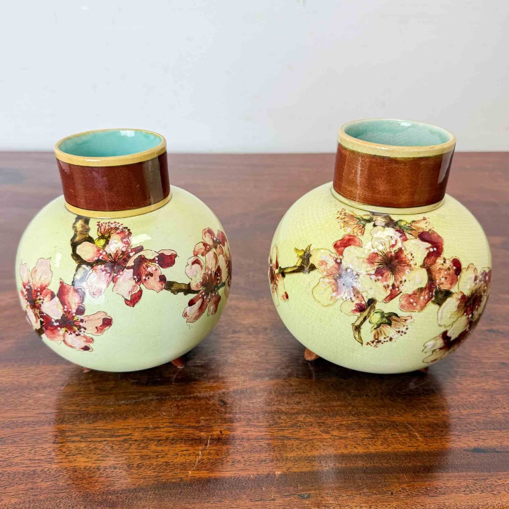 A pair of round pale green ceramic vases with hand-painted pink cherry blossom branches, dark brown collars, and small tripod feet. View II