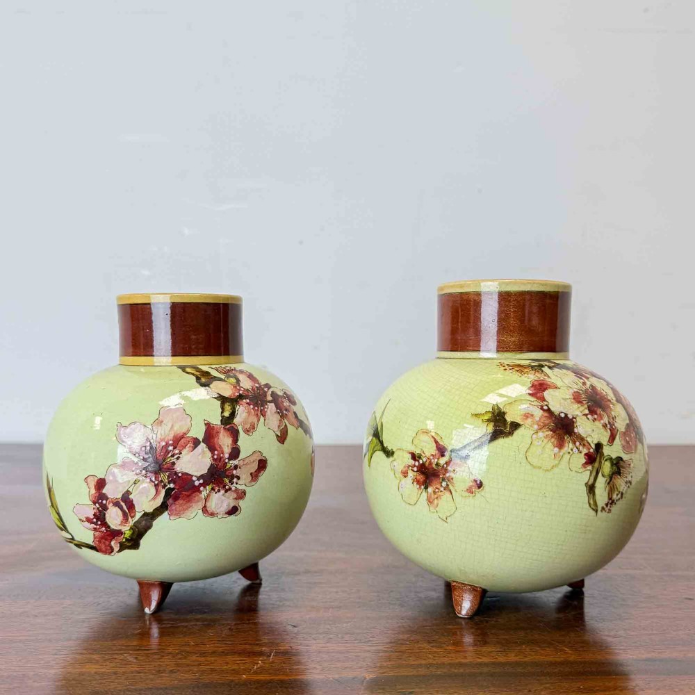 A pair of round pale green ceramic vases with hand-painted pink cherry blossom branches, dark brown collars, and small tripod feet. View V