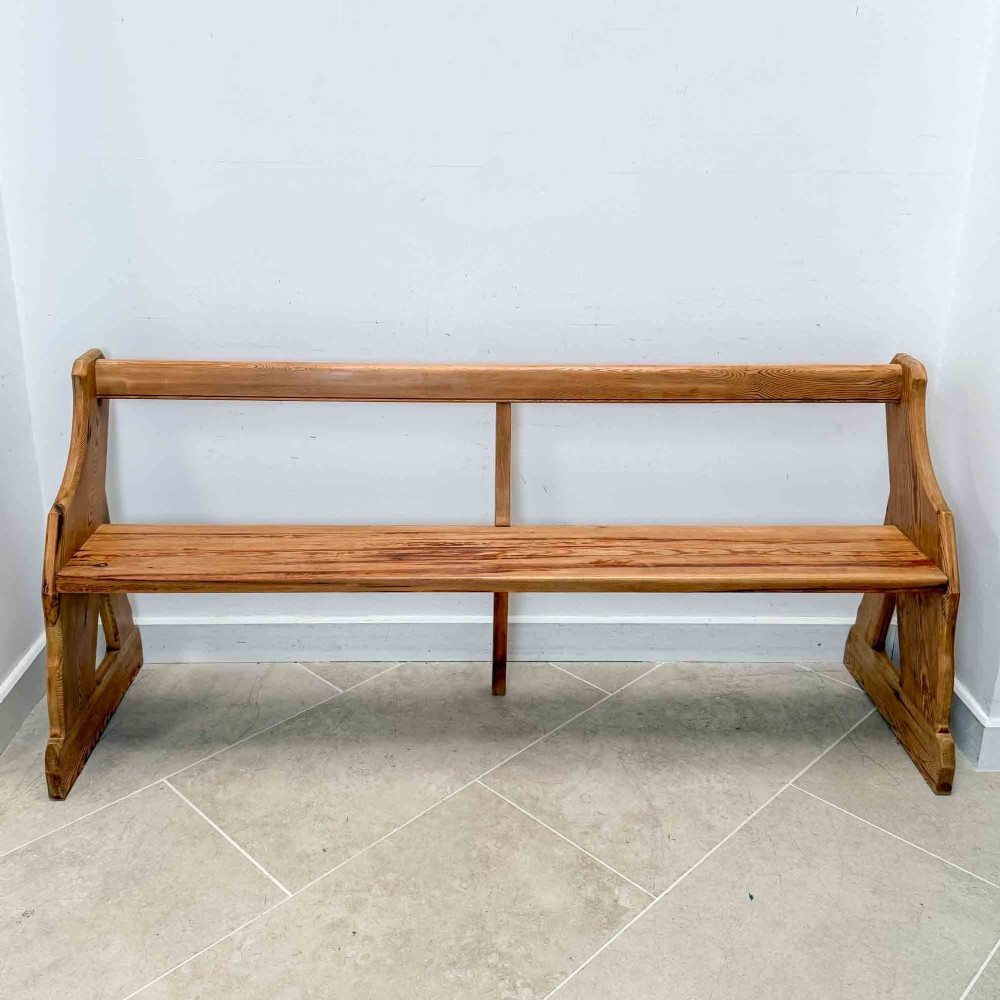 An antique pitch pine open back church pew featuring shaped side supports and a single central back support. View II