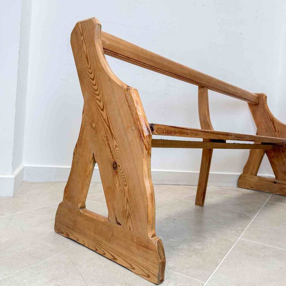 An antique pitch pine open back church pew featuring shaped side supports and a single central back support. View IV