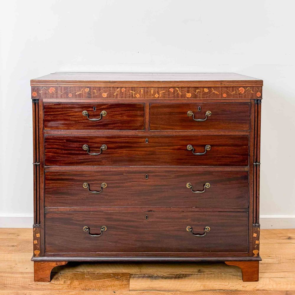 An antique mahogany chest of drawers with two short over three long drawers and floral inlay details along the upper frieze.