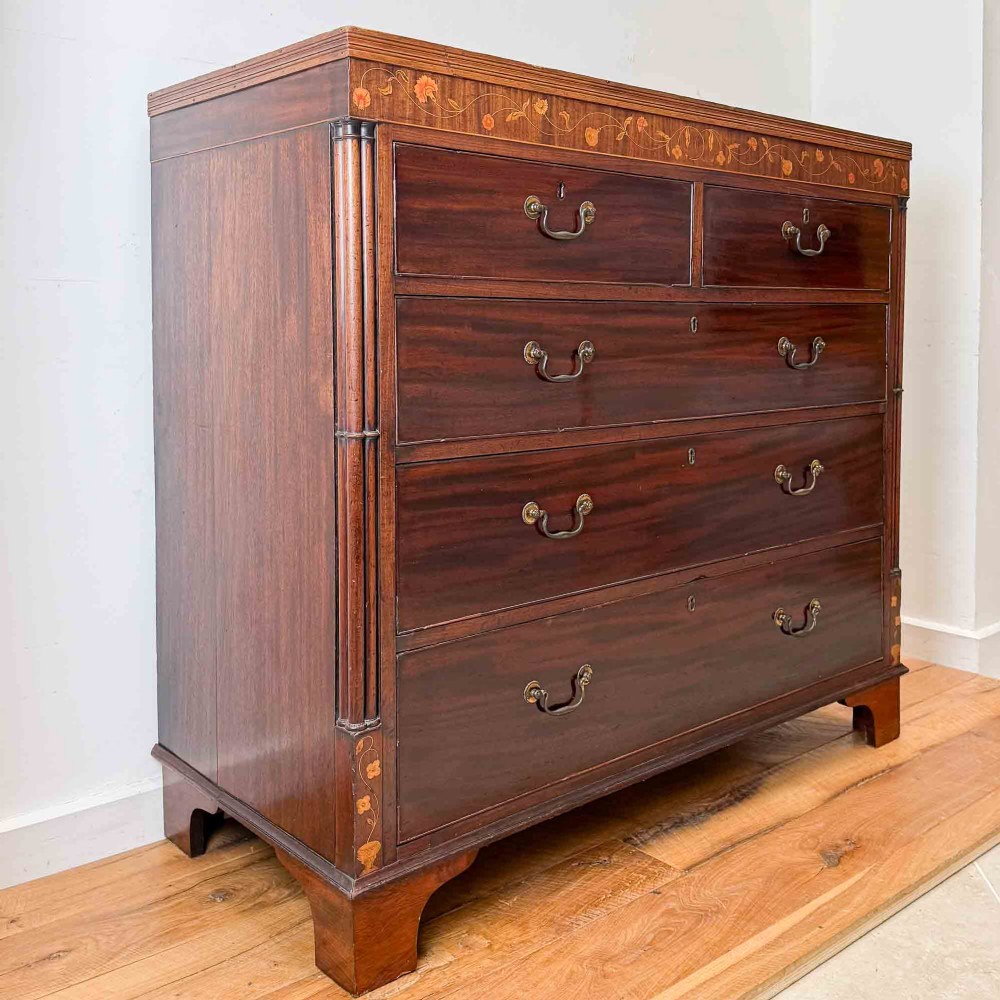 An antique mahogany chest of drawers with two short over three long drawers and floral inlay details along the upper frieze. View II