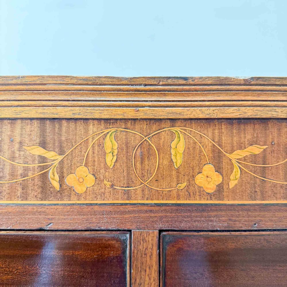 An antique mahogany chest of drawers with two short over three long drawers and floral inlay details along the upper frieze. View IV