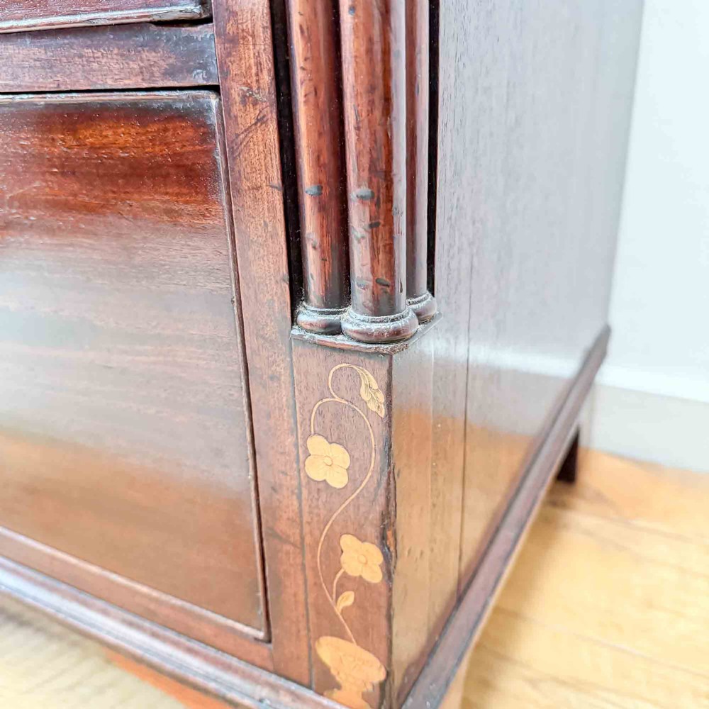 An antique mahogany chest of drawers with two short over three long drawers and floral inlay details along the upper frieze. View V