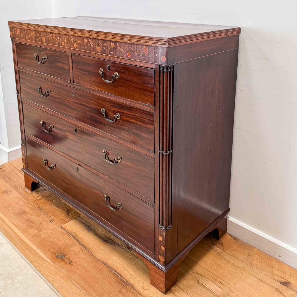 An antique mahogany chest of drawers with two short over three long drawers and floral inlay details along the upper frieze. View VI