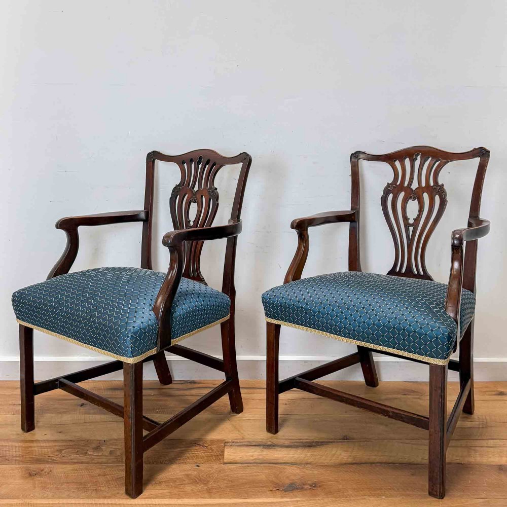 A pair of dark mahogany armchairs featuring carved pierced back splats, shaped arms, and blue patterned upholstered seats.