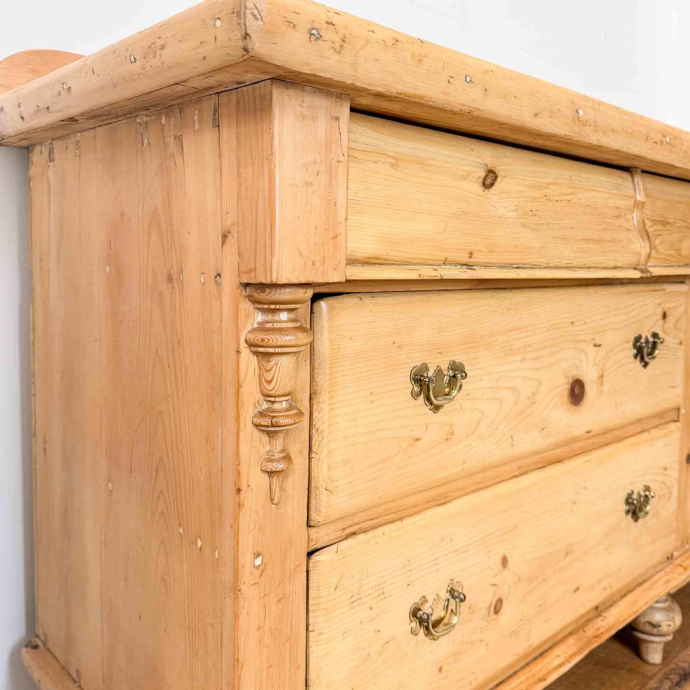 A Victorian natural pine dresser base featuring a low upstand back, seven drawers with metal drop handles, and turned bun feet. View III