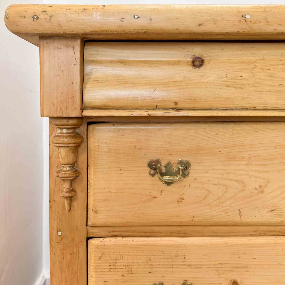 A Victorian natural pine dresser base featuring a low upstand back, seven drawers with metal drop handles, and turned bun feet. View IV