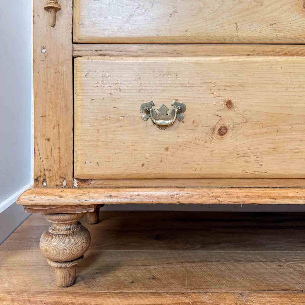 A Victorian natural pine dresser base featuring a low upstand back, seven drawers with metal drop handles, and turned bun feet. View V