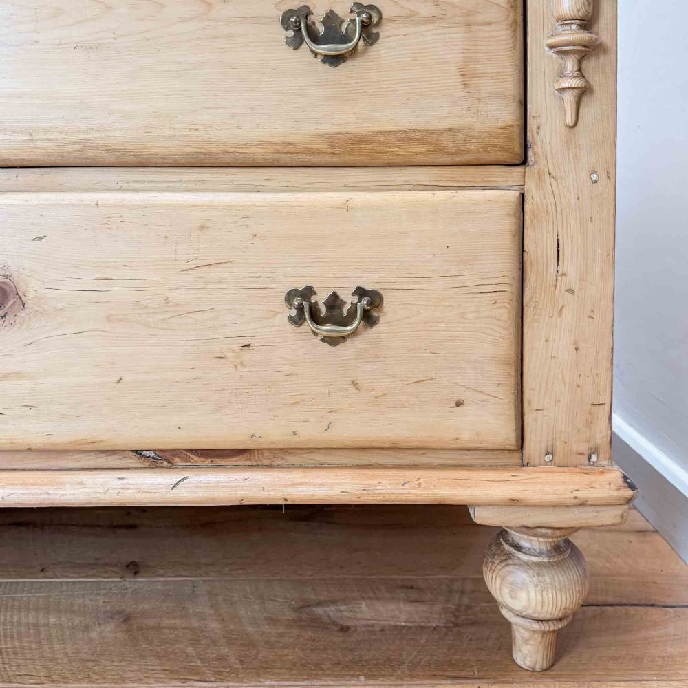 A Victorian natural pine dresser base featuring a low upstand back, seven drawers with metal drop handles, and turned bun feet. View VI