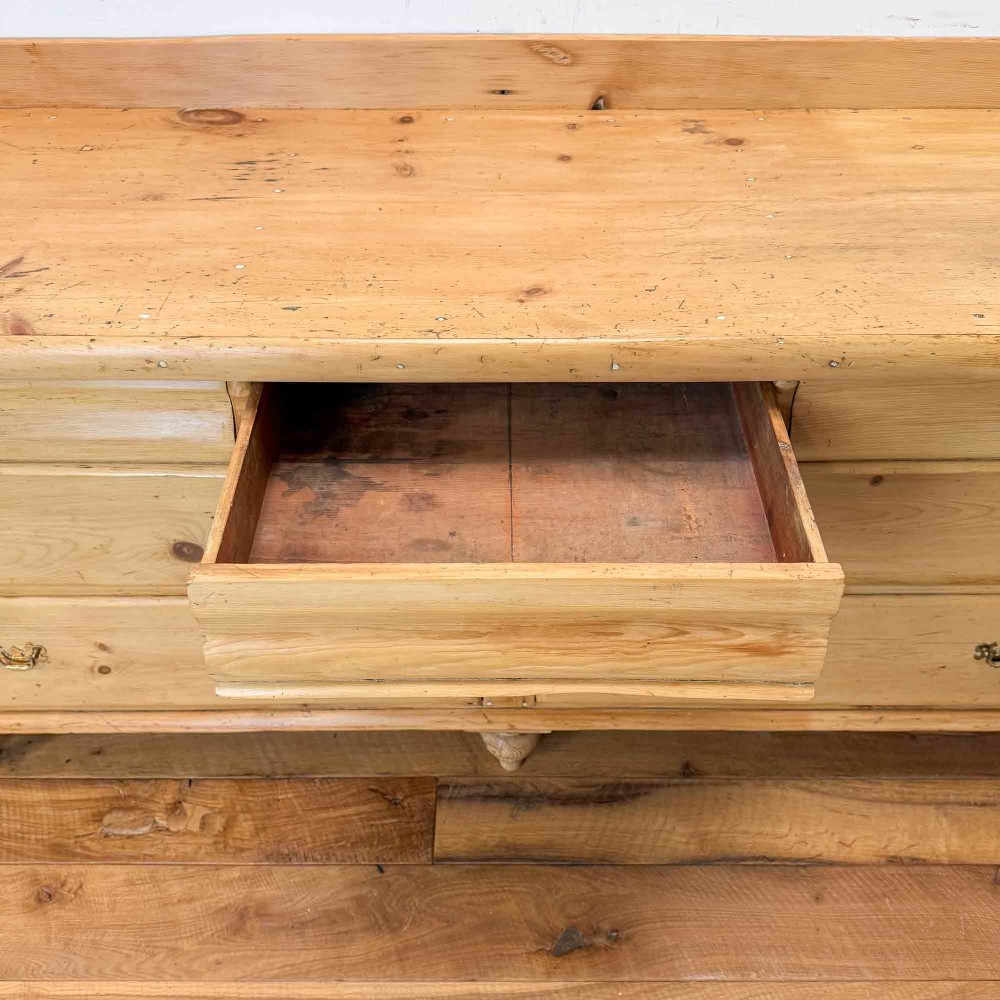 A Victorian natural pine dresser base featuring a low upstand back, seven drawers with metal drop handles, and turned bun feet. View VII