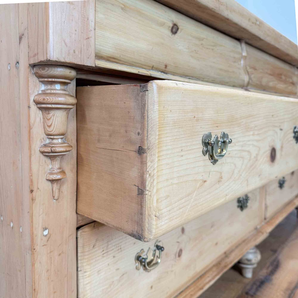 A Victorian natural pine dresser base featuring a low upstand back, seven drawers with metal drop handles, and turned bun feet. View VIII