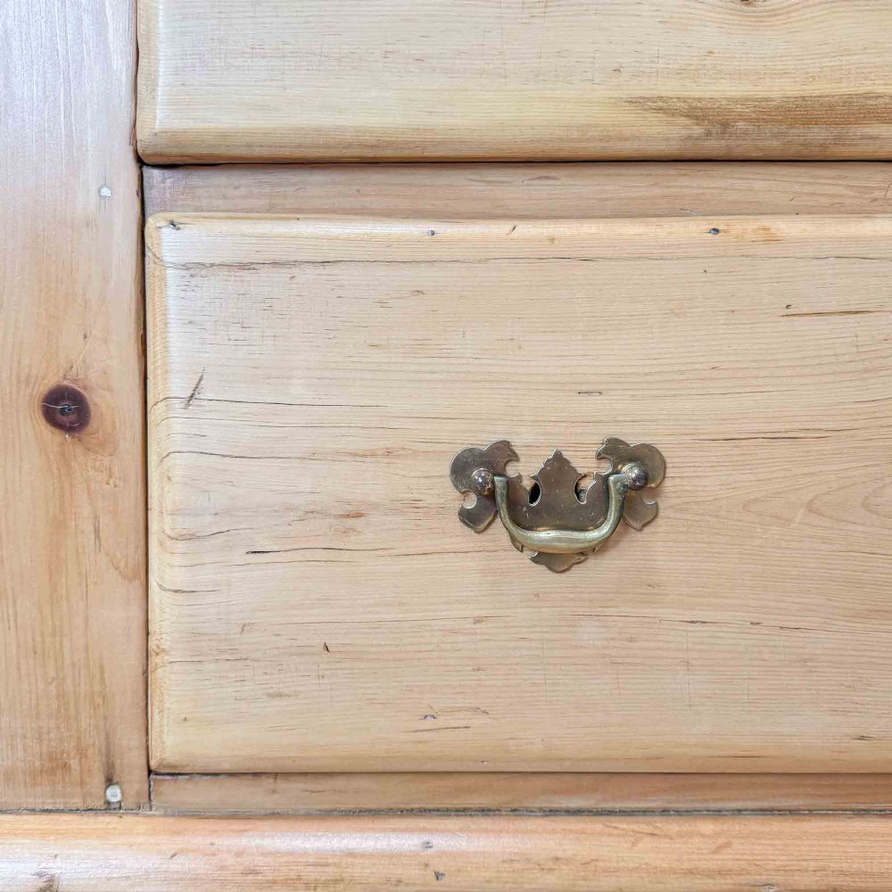 A Victorian natural pine dresser base featuring a low upstand back, seven drawers with metal drop handles, and turned bun feet. View X