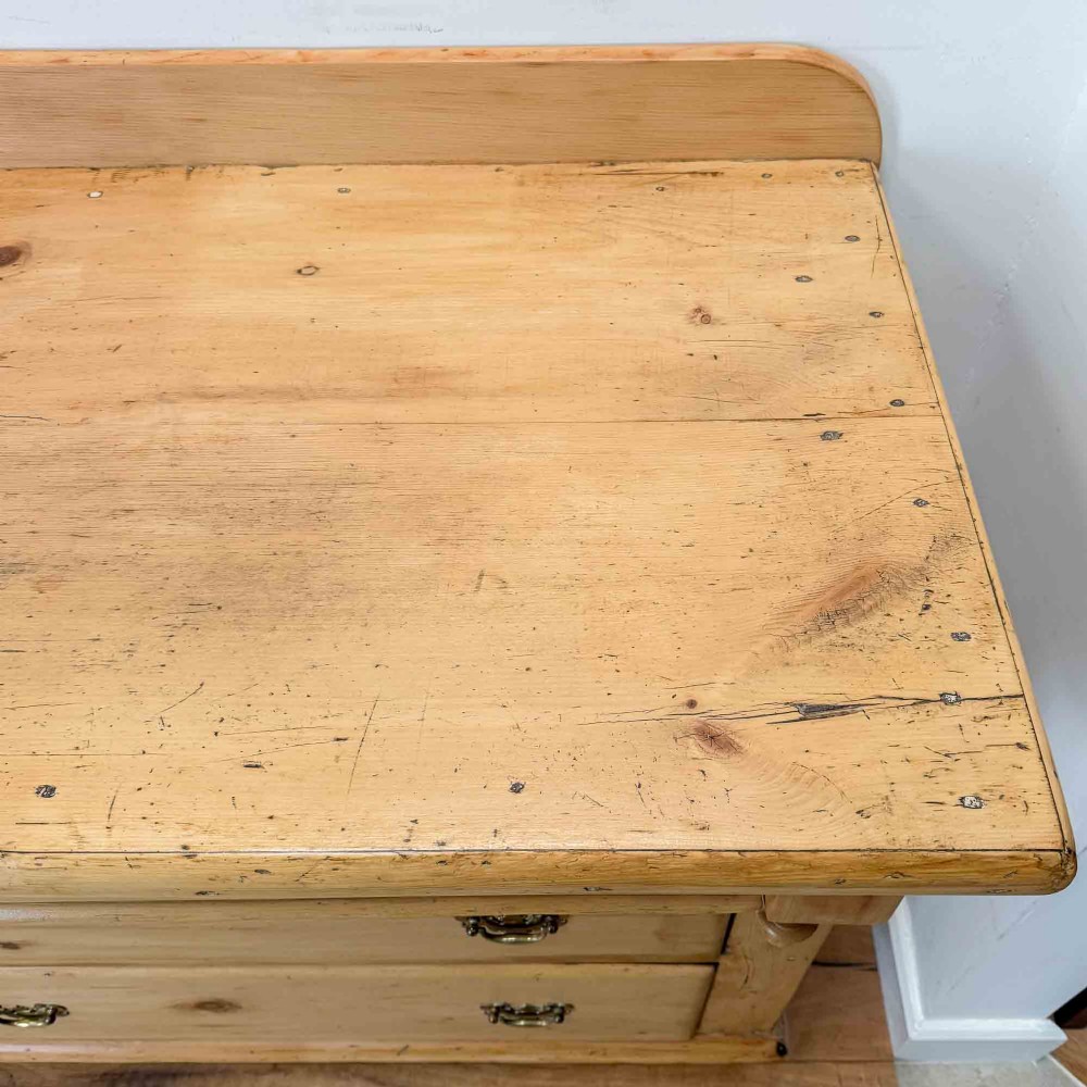 A Victorian natural pine dresser base featuring a low upstand back, seven drawers with metal drop handles, and turned bun feet. View XI